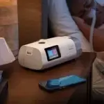 AirCurve 11 ASV PaceWave laite yöpöydällä kuvattuna, vieressä nukkuva käyttäjä ja älypuhelin.