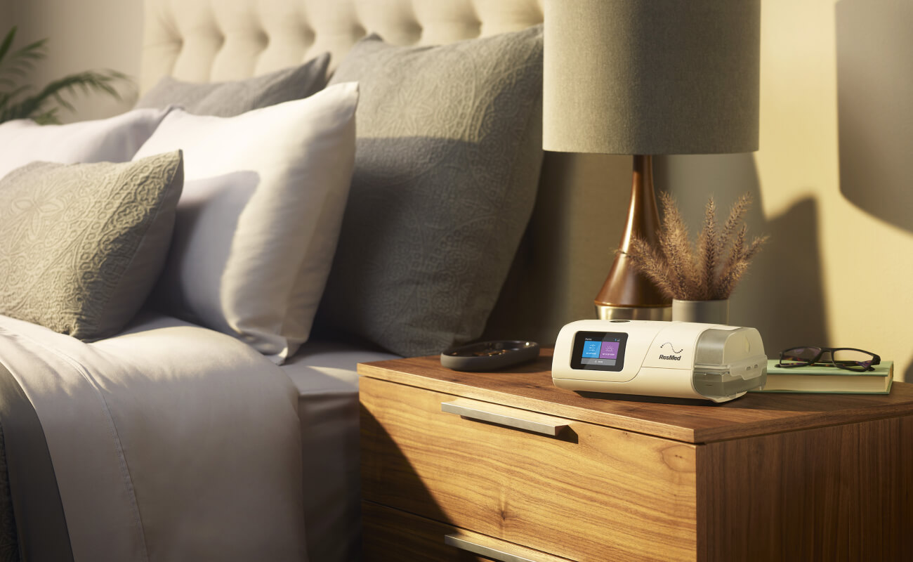 AirCurve 11 ASV PaceWave adaptiivinen servoventilaattori kuvattuna yöpöydällä, jossa on lamppu, lukulasit ja kirja.